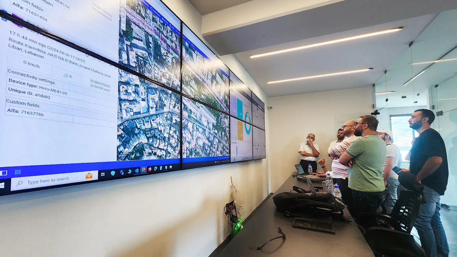 A group of people in a control room monitoring a fleet management telematics system. The wall-sized display shows GPS-based tracking data and satellite imagery of vehicles in Beirut, Lebanon, along with system dashboards and analytics. How to measure digital product analytics for business teams, in plain terms